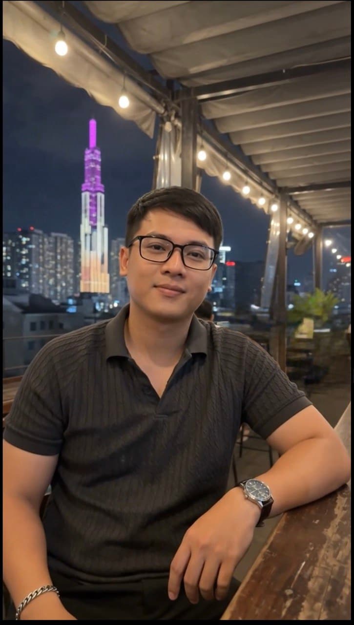Khoa seated at an evening rooftop venue with the city behind him