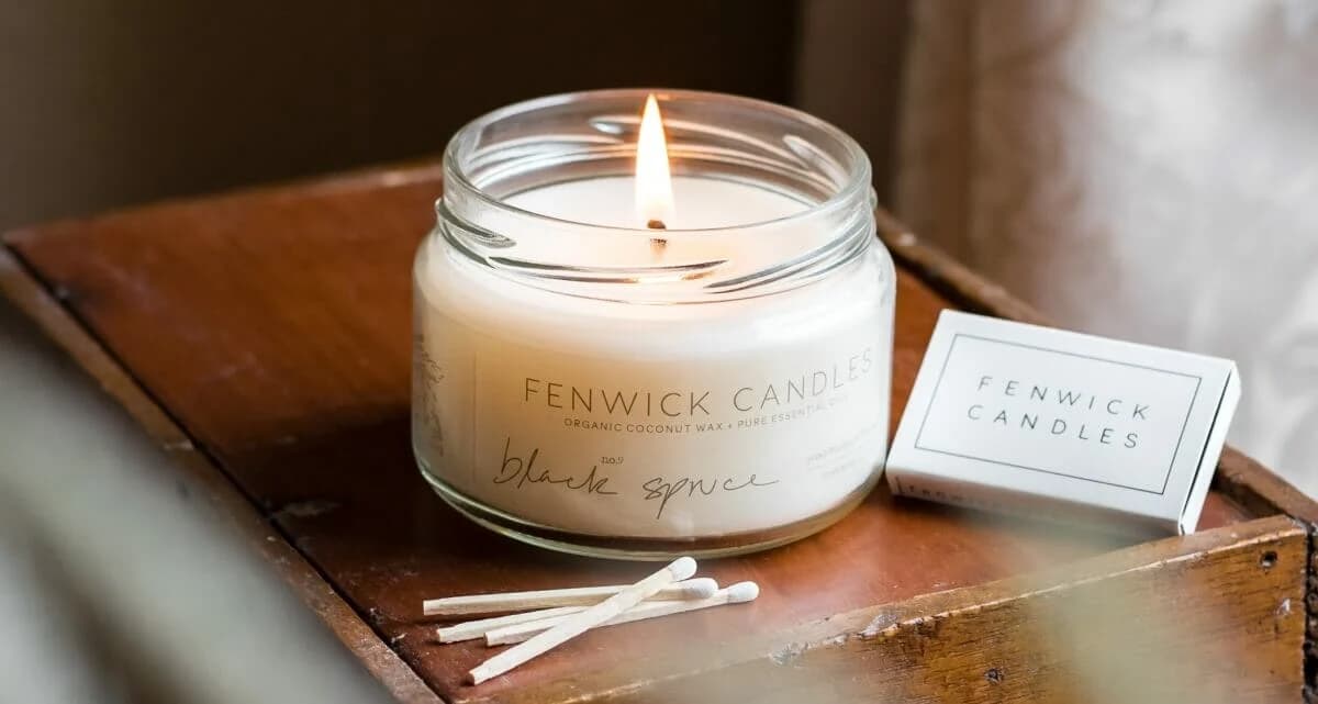 A lit Fenwick candles glass jar beside wooden matches on a table
